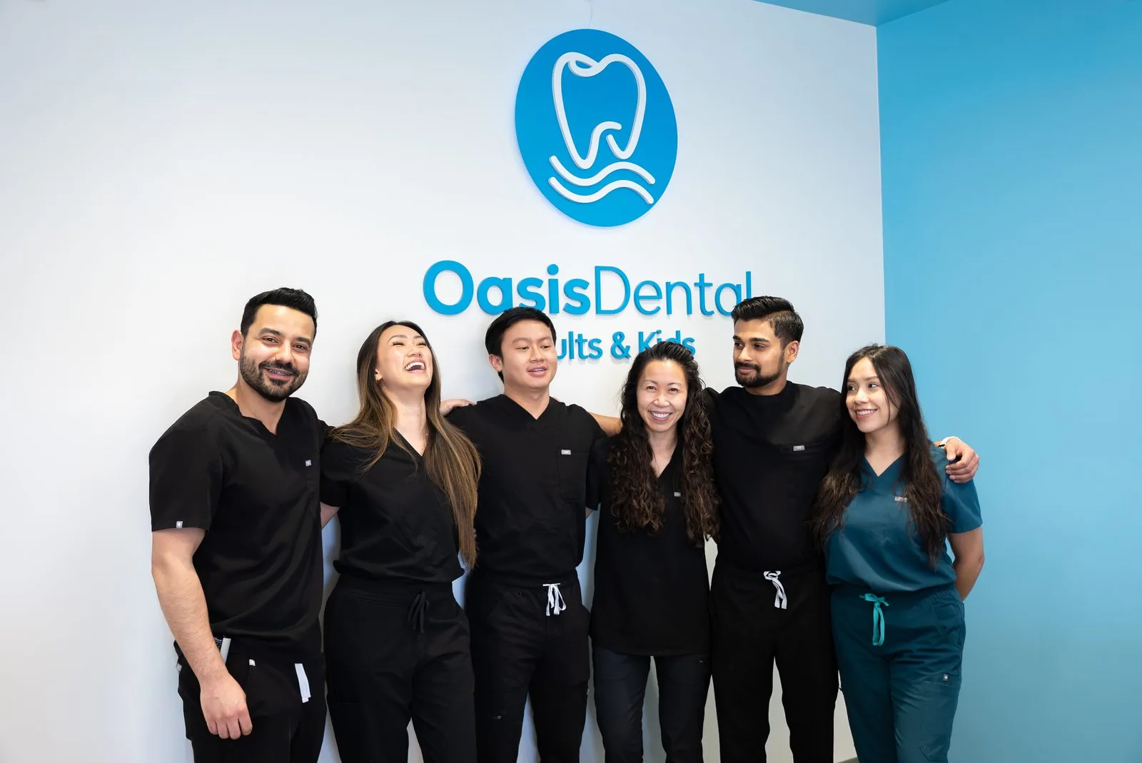 Oasis Dental team laughing together in front of the logo wall