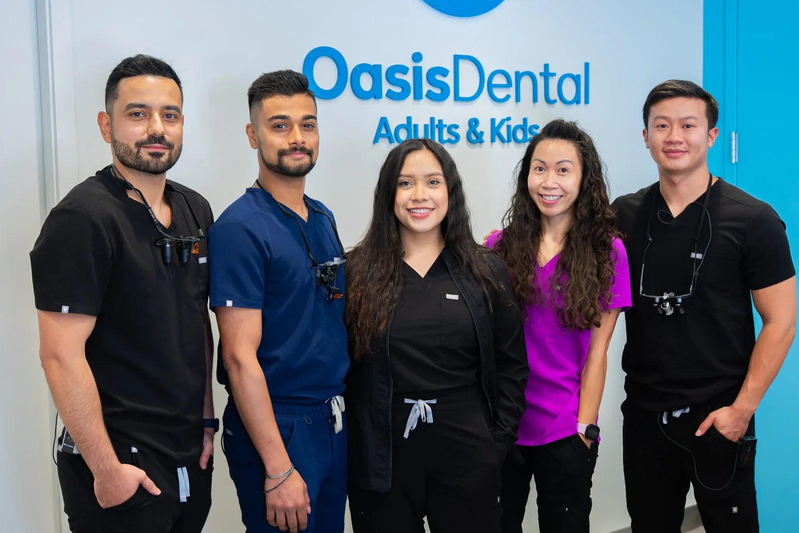 Five Oasis Dental doctors wearing dental loupes in front of the Adults & Kids sign
